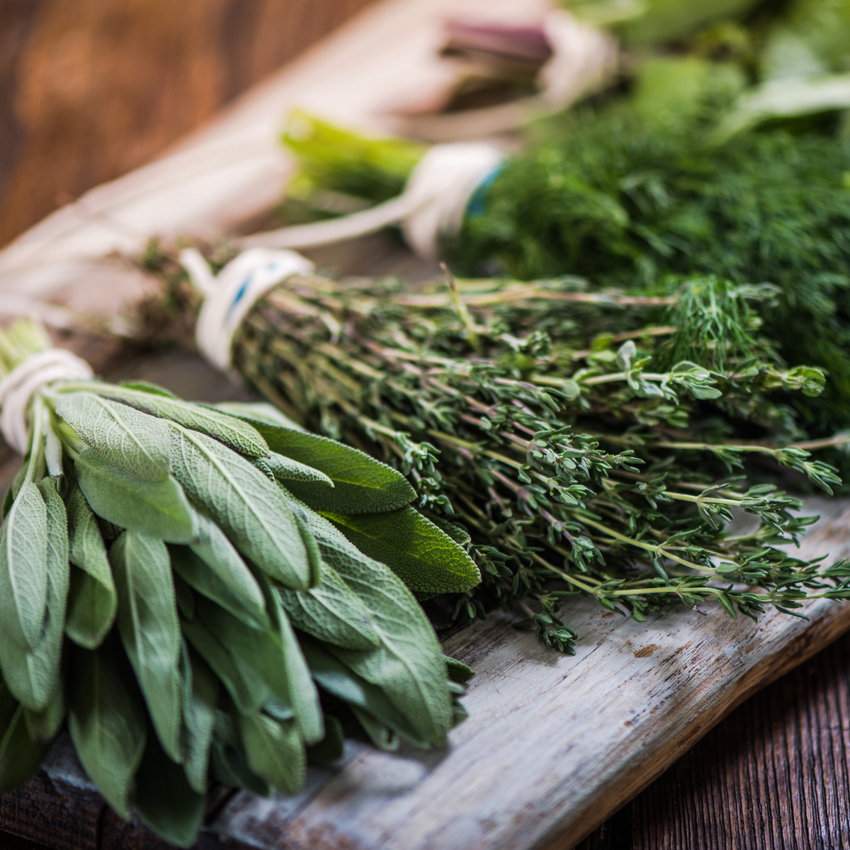 "Herbs for healthy skin" image with turmeric, rosemary, basil, and cilantro on a wooden surface.