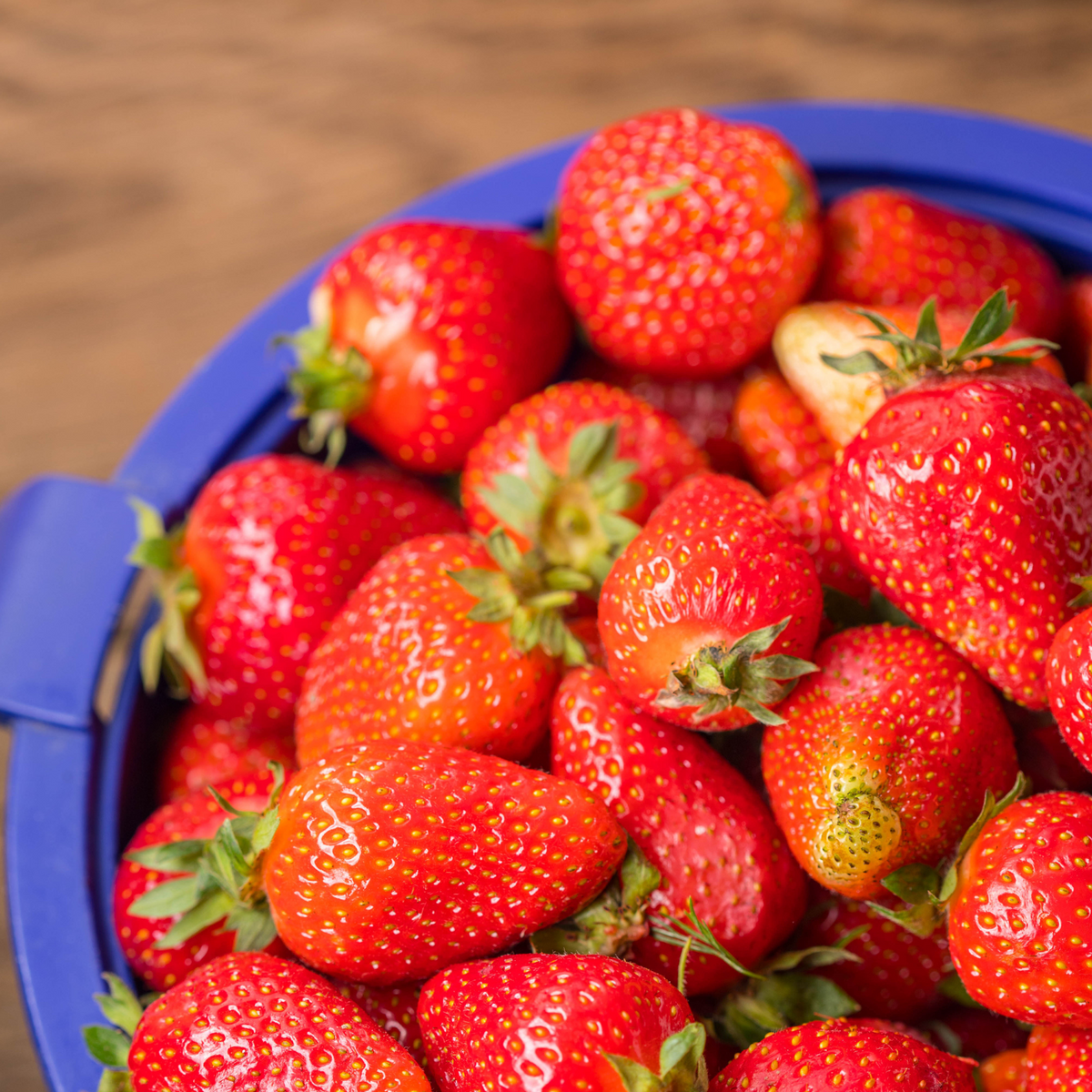 The image depicts a close-up of plump, red strawberries nestled among green leaves on a sun-drenched day.